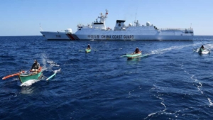 Filipino fishermen aboard their wooden boats sailing past a Chinese coast guard ship near the China-controlled Scarborough Shoal, in disputed waters of the South China Sea. Photo by TED ALJIBE / AFP